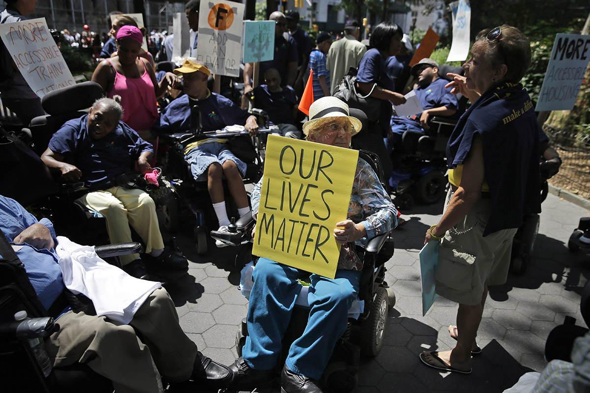 Anita Cantor, in a wheelchair, holds a sign that reads "Our Lives Matter" during the inaugural Disability Pride Parade in New York. Around her, other with disabilities hold signs calling more elevators at train stations and more accessible housing